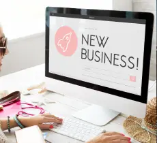 A person wearing sunglasses types on a computer with a "New Business!" website displayed on the screen